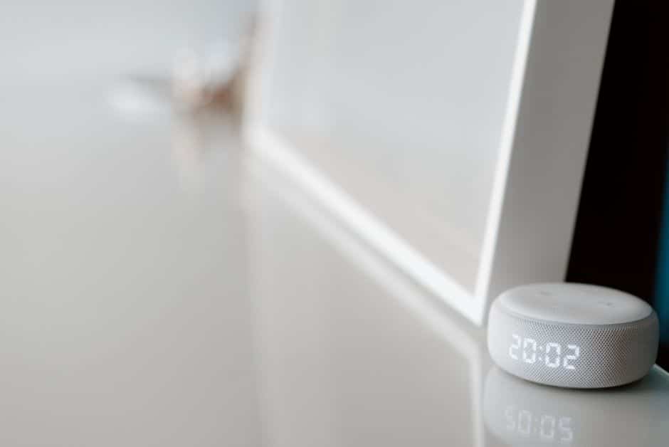 A smart speaker with a clock display on a shelf