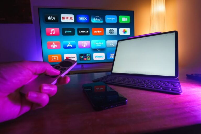 A hand holding an Apple TV remote with the streaming home screen visible