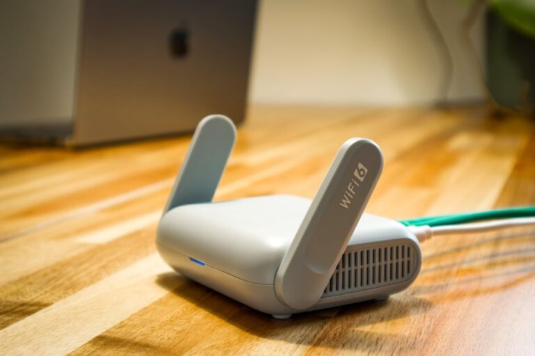 A Wi-Fi 6 router plugged in on a wooden floor next to a laptop